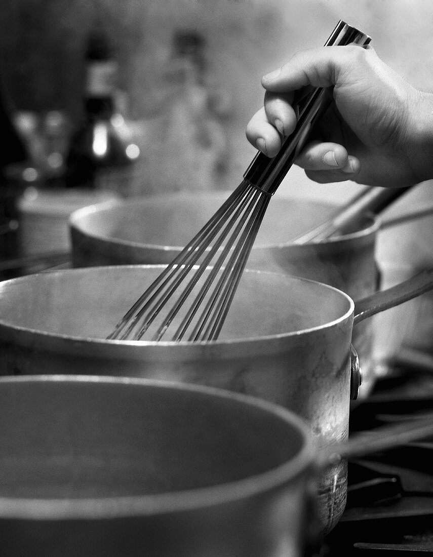 A Hand Using a Whisk in a Steaming Saucepan