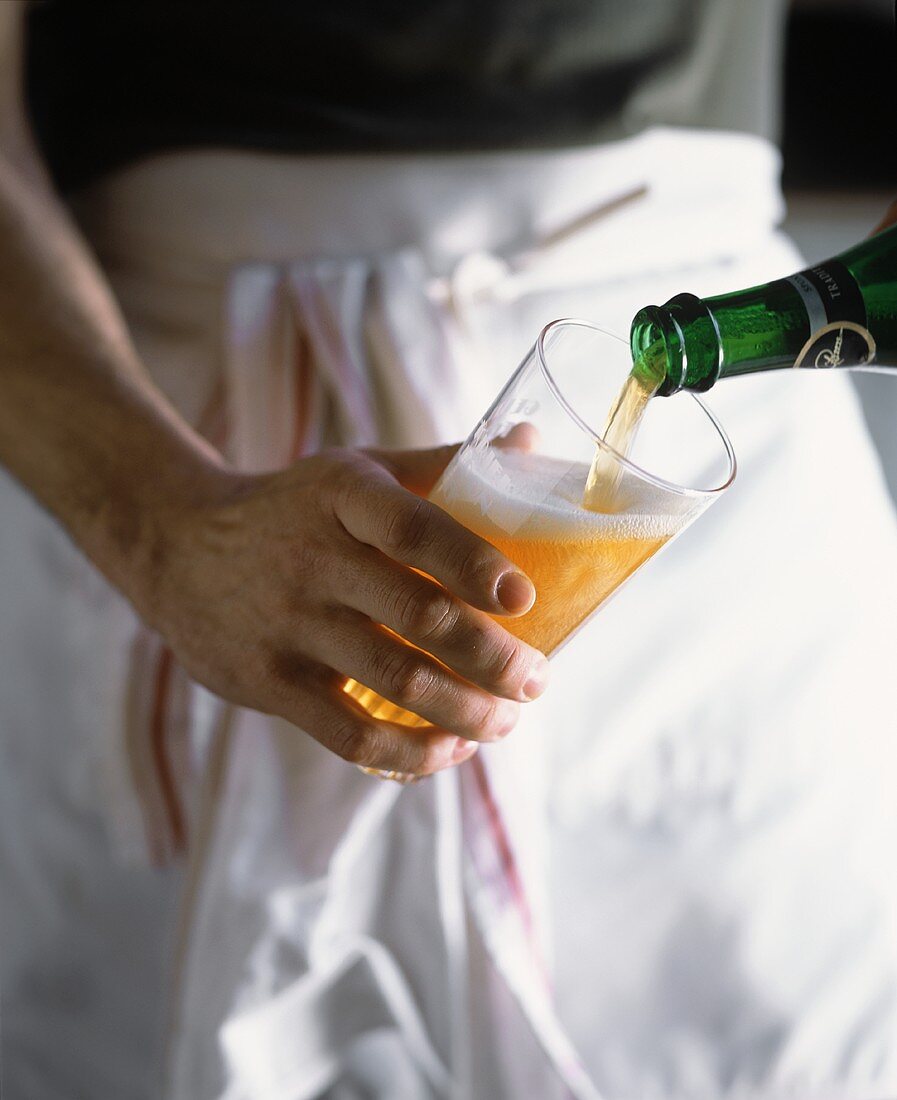 Man Wearing White Apron Pouring Beer from Bottle into Glass