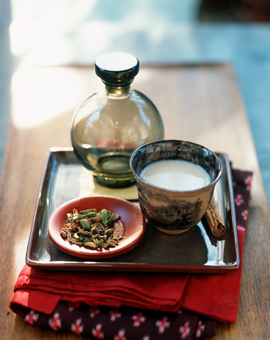 Chai Tee in asiatischem Schälchen und Teeblätter auf Tablett