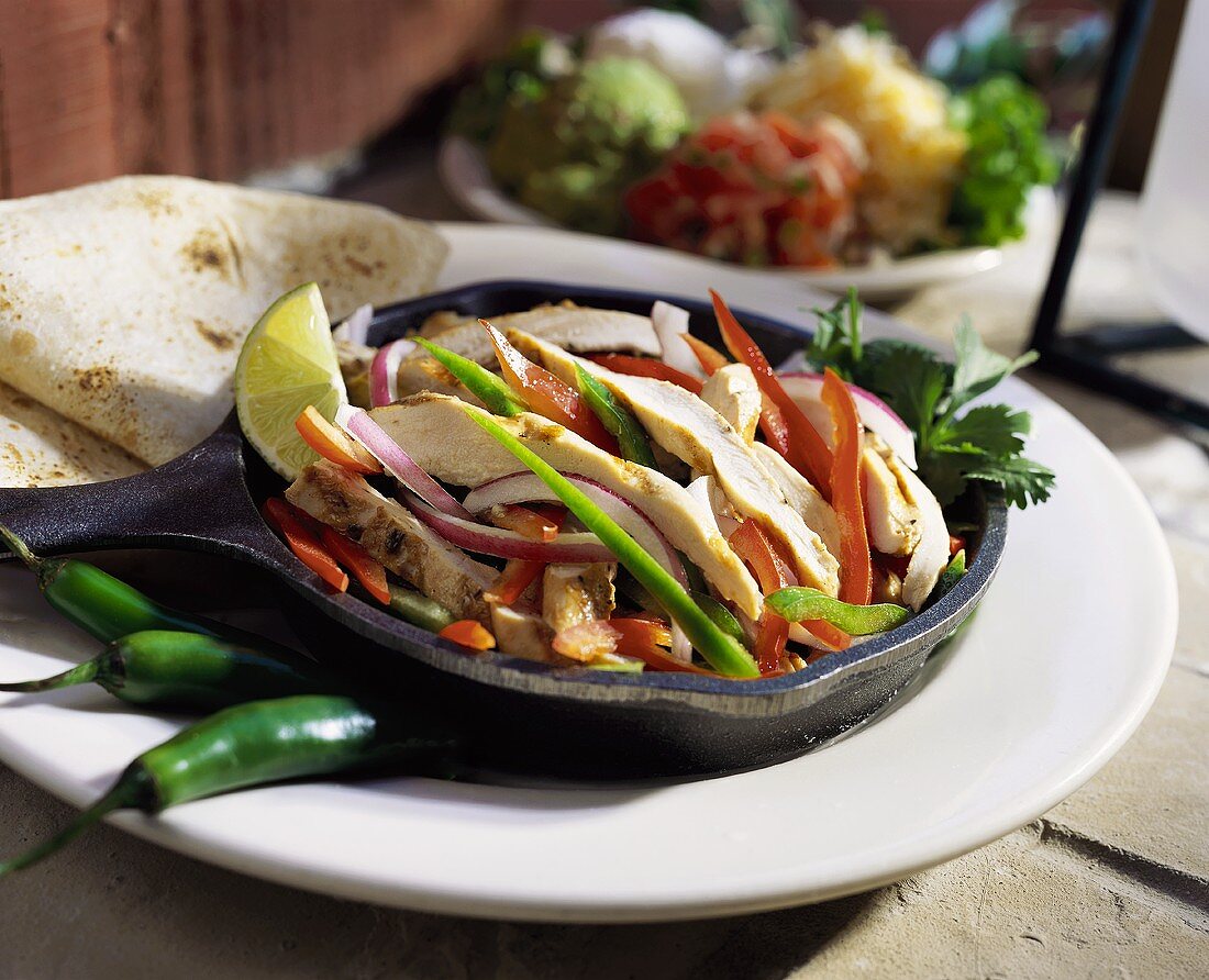 Strips of chicken & peppers in cast-iron frying pan; tortillas