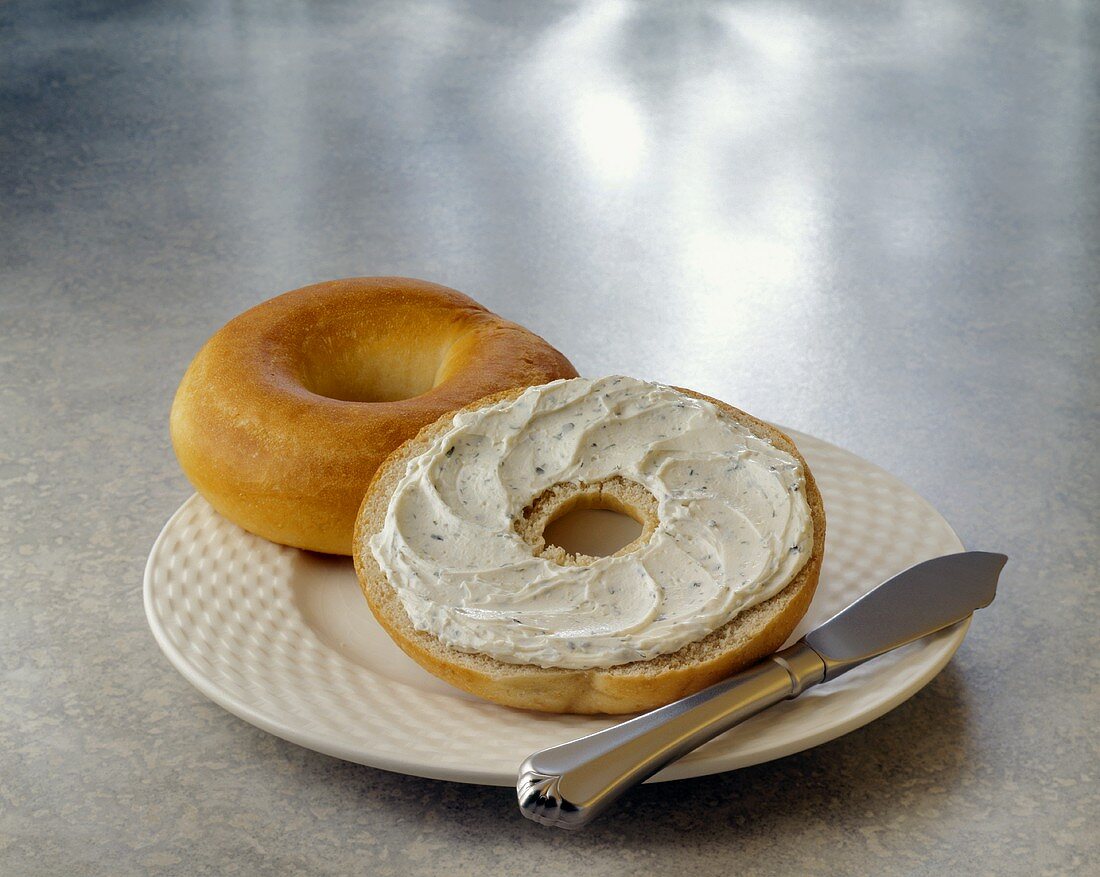 Bagel mit Kräuterfrischkäse auf Teller mit Messer