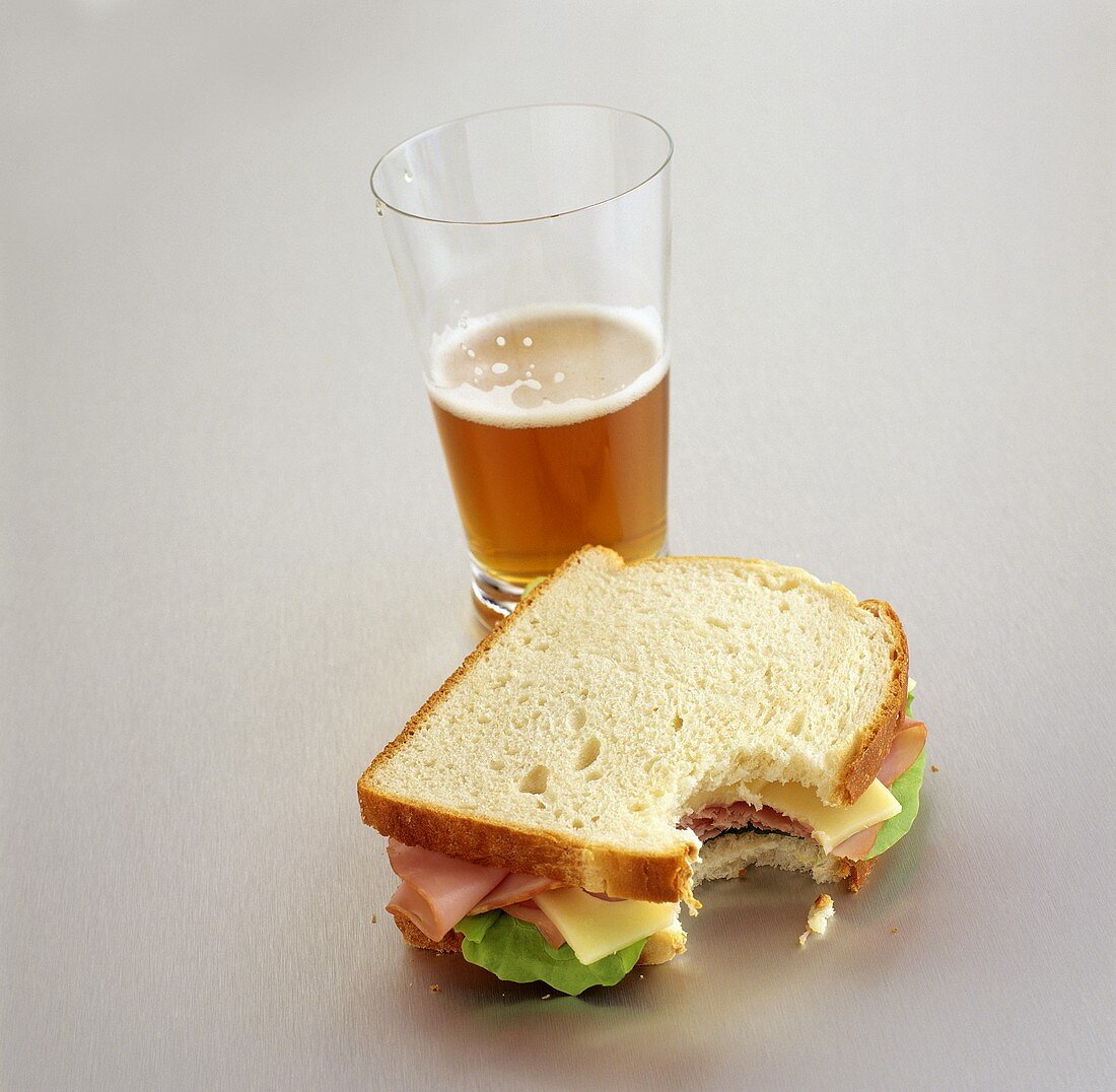 Schinken-Käse-Sandwich, angebissen; Glas Bier