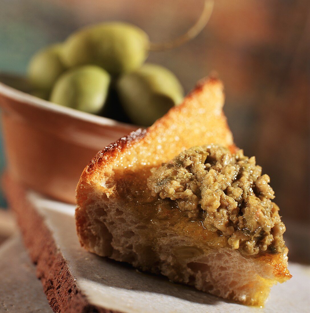 Tapenade aus grünen Oliven auf Brotstück (Nahaufnahme)