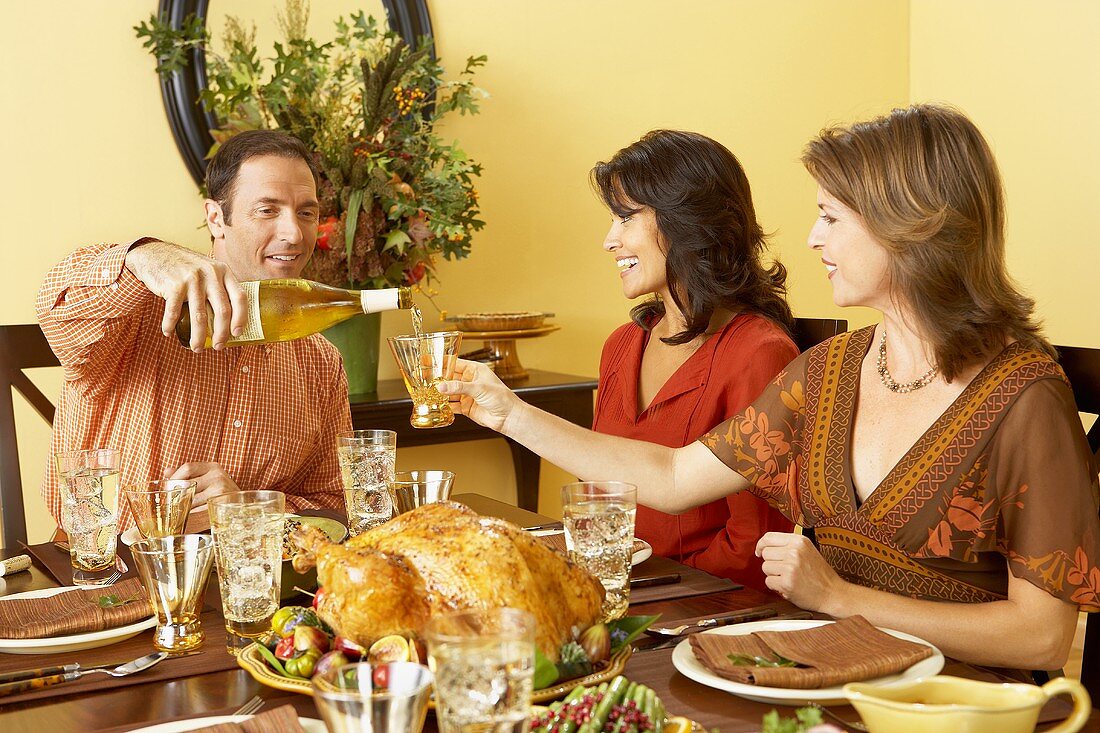 Mann giesst Frau Weißwein ins Glas beim Thanksgiving-Essen