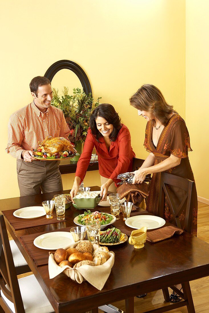 Man and Women Setting Thanksgiving Table, Man Holding Platter of Roasted Turkey