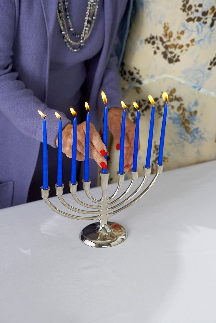 Frau steckt blaue Kerze in Kerzenleuchter zu Hannukah