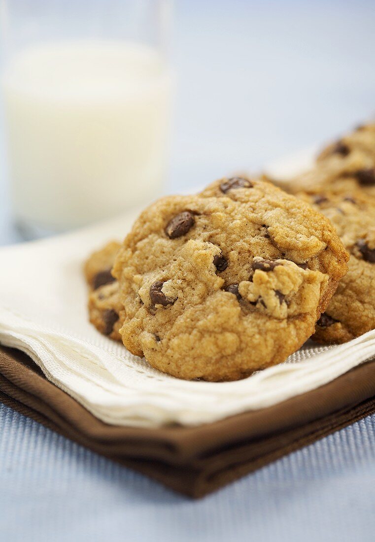 Chocolate Chip Cookies auf Serviette, dahinter Glas Milch