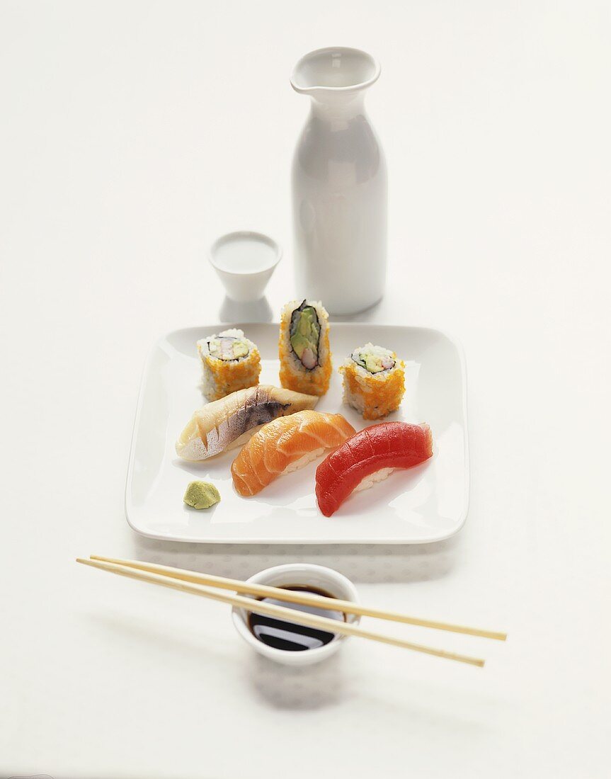 Assorted Sushi on a Square White Plate; Chopsticks with Soy Sauce; Sake
