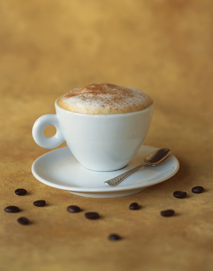 Tasse Cappuccino und verstreute Kaffeebohnen