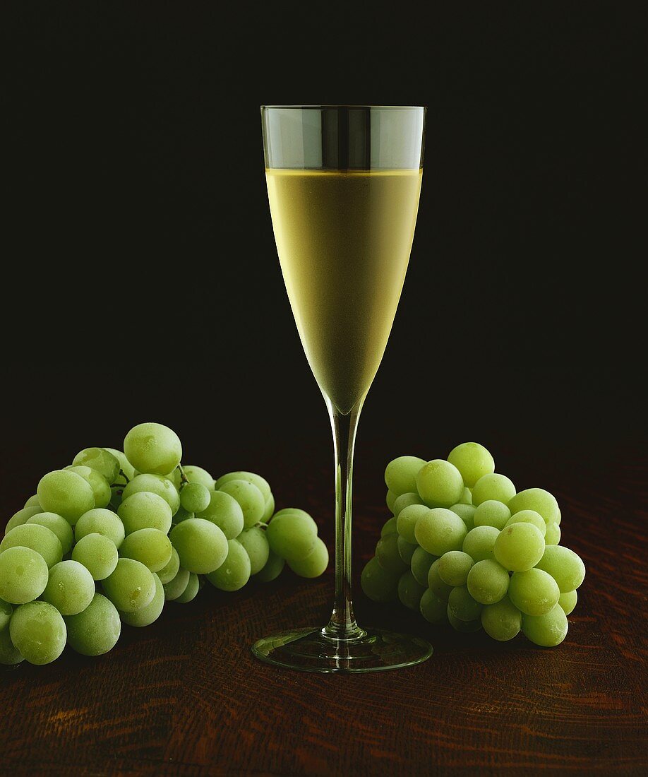 Glas Weißwein umgeben von grünen Trauben