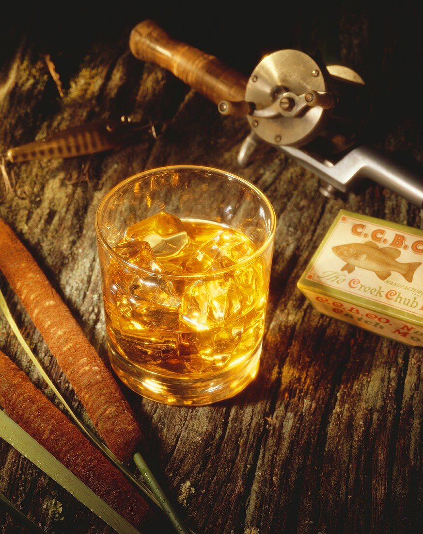 Glass of Scotch on the Rocks with Fishing Pole and Cattail on a Log