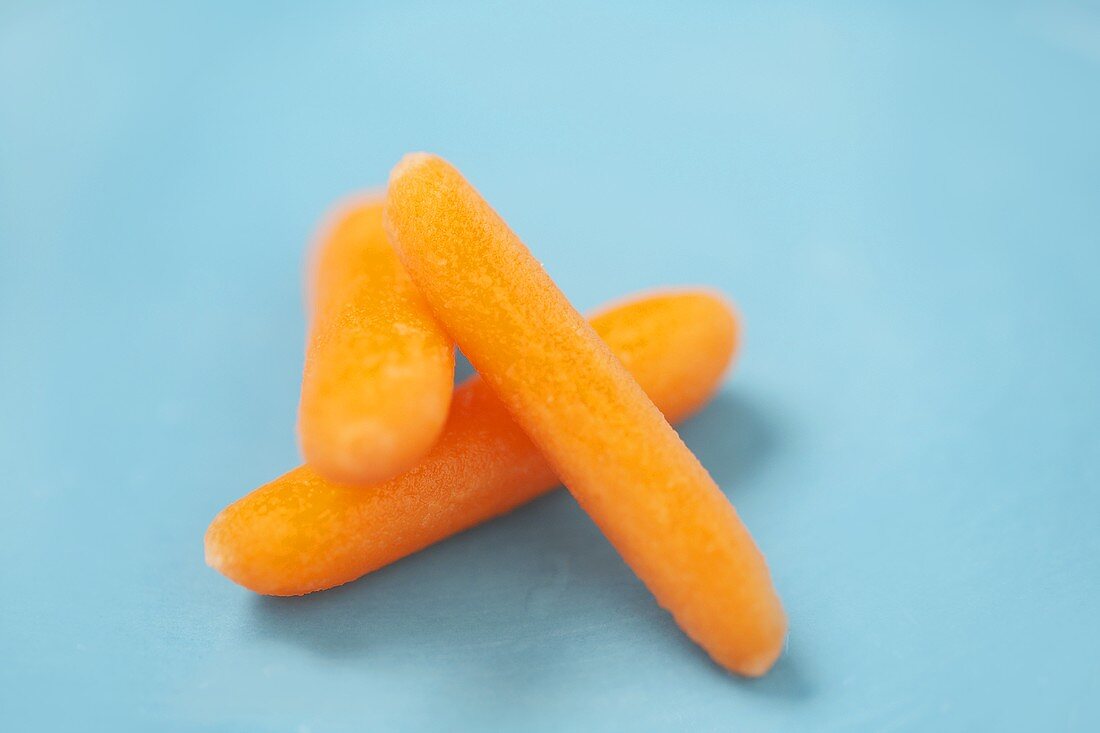 Close Up of Three Baby Carrots on a Blue Background