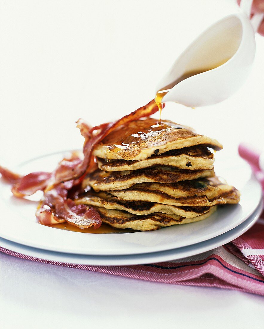 Pouring Maple Syrup Over a Stack of Blueberry Pancakes with Bacon