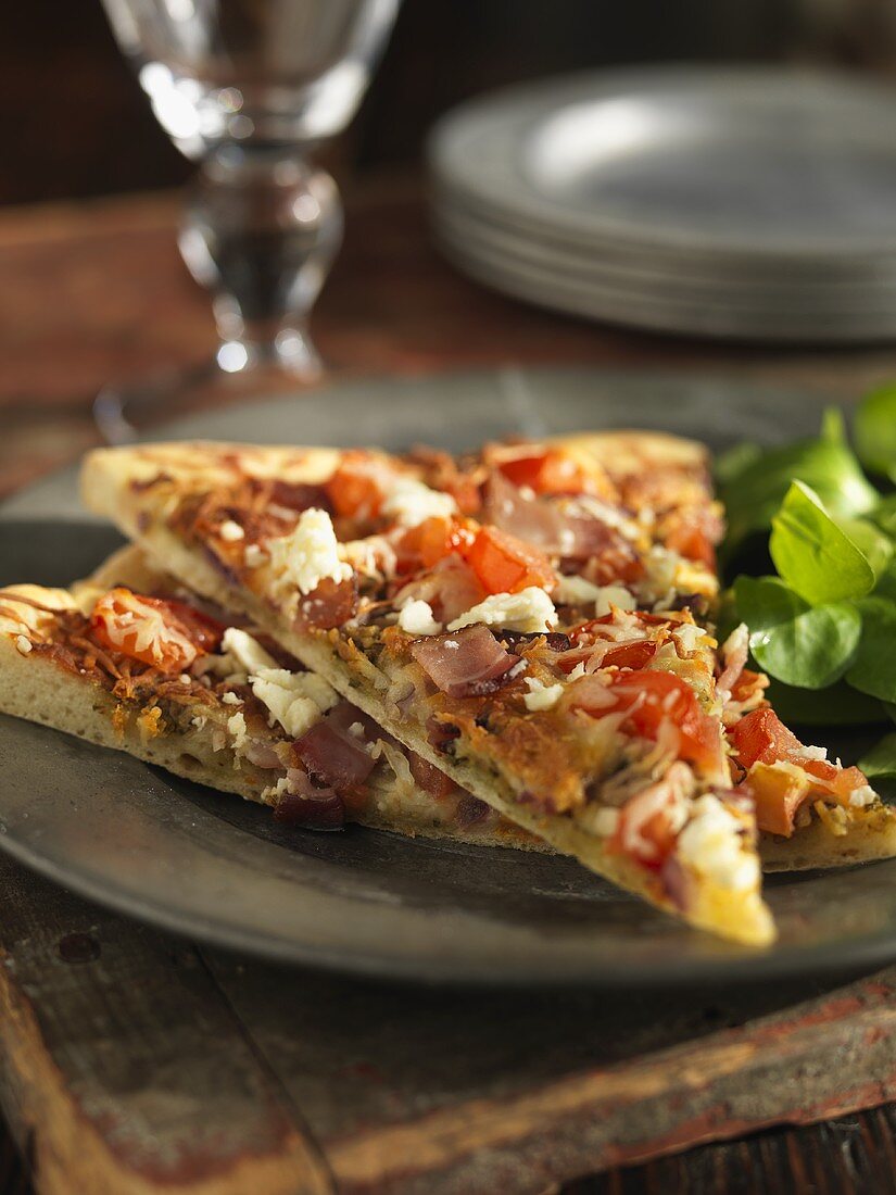 Pizzastücke mit Tomaten, Feta, Schinken und roten Zwiebeln