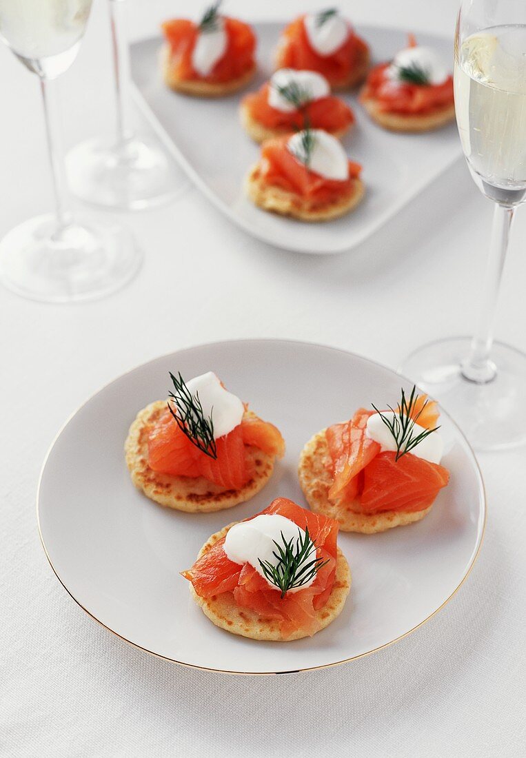 Blinis mit Räucherlachs auf Tellern, dazu Sekt in Gläsern