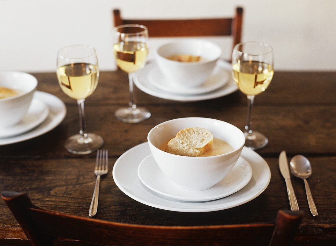 Table Set with Bowls of Lobster Bisque Topped with Bread; White Wine