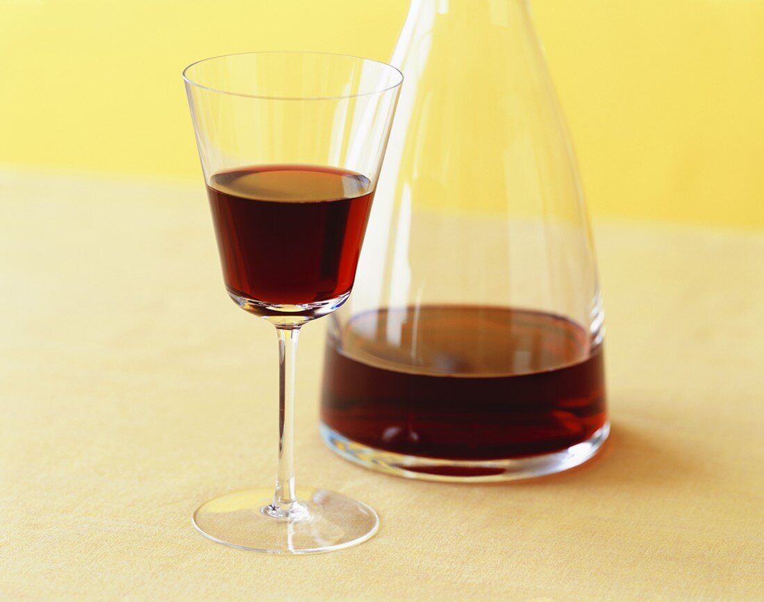 A Glass and Carafe of Red Wine on Yellow Background
