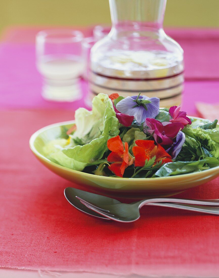 Salat mit essbaren Blüten auf gelbem Teller