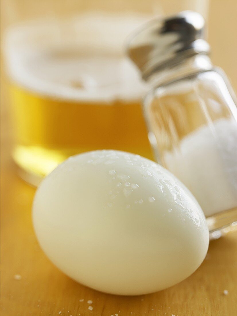 Hartgekochtes Ei mit Salzstreuer vor Glas Bier