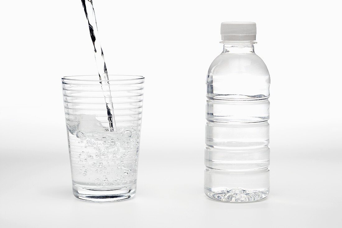 Wasser in Glas einschenken, daneben Wasserflasche