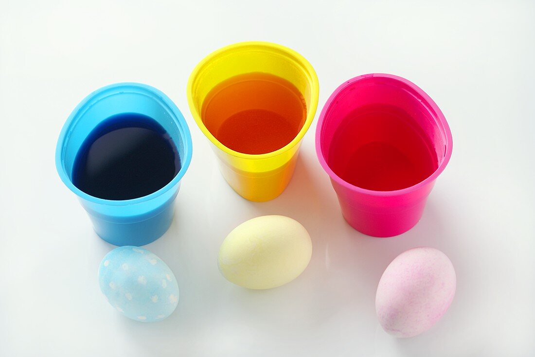 Drei gefärbte Eier neben Becher mit Eierfarben