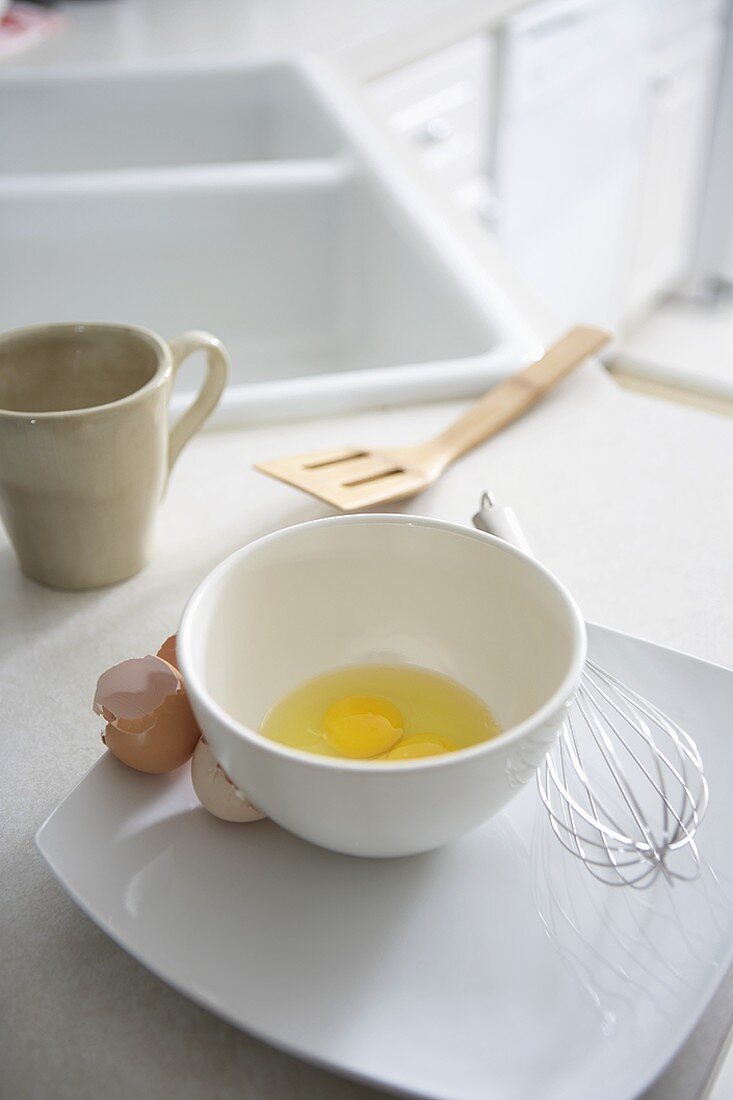 Aufgeschlagene Eier, Eierschalen und Schneebesen in Küche