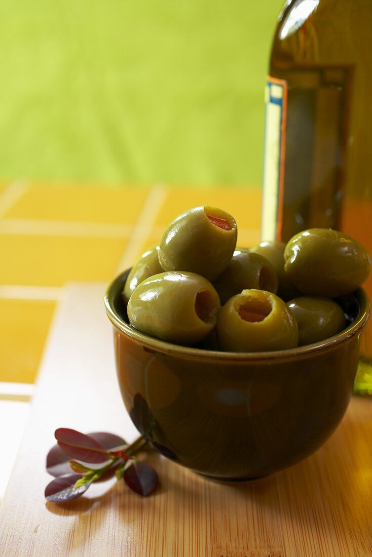 Grüne Bio-Oliven in Schale, Flasche Olivenöl im Hintergrund