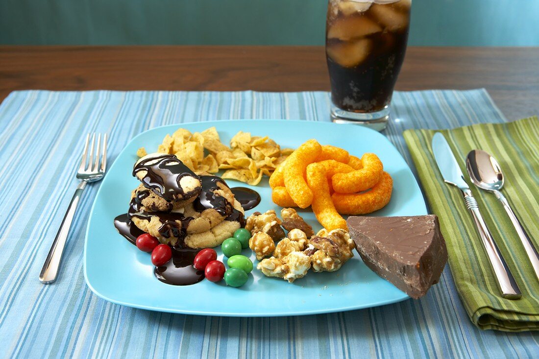 Junk Food auf Teller, Glas Cola im Hintergrund