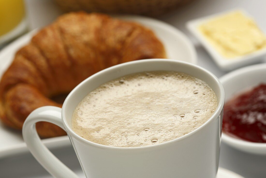 Tasse Kaffee mit Milchschaum, Croissant, Marmelade, Butter