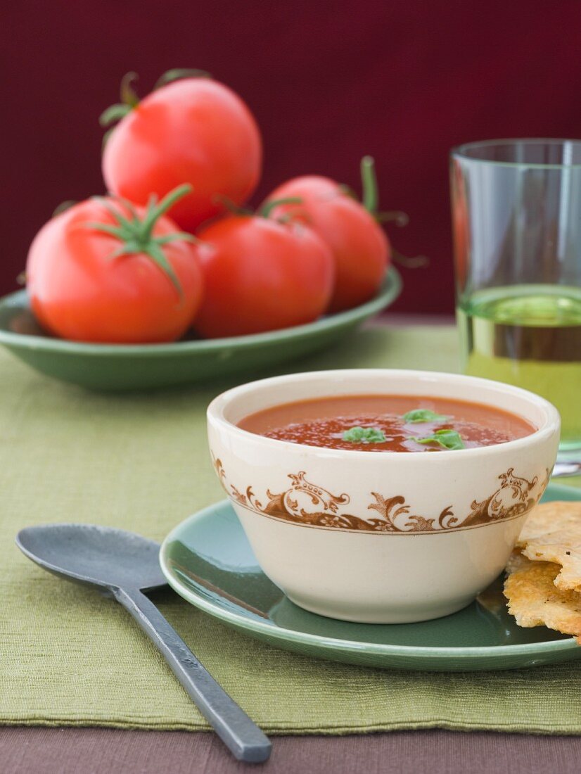 Tomatensuppe im Schälchen, im Hintergrund frische Tomaten