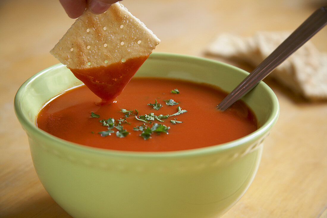 Hand dipping a cracker in tomato soup