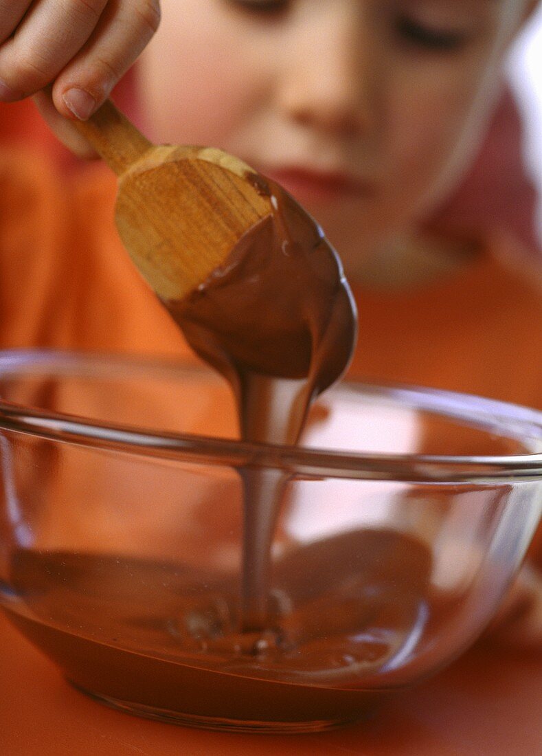 Small girl stirring chocolate cream with wooden spoon