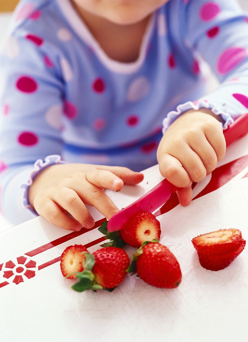 Mädchen schneidet Erdbeere mit Plastikmesser