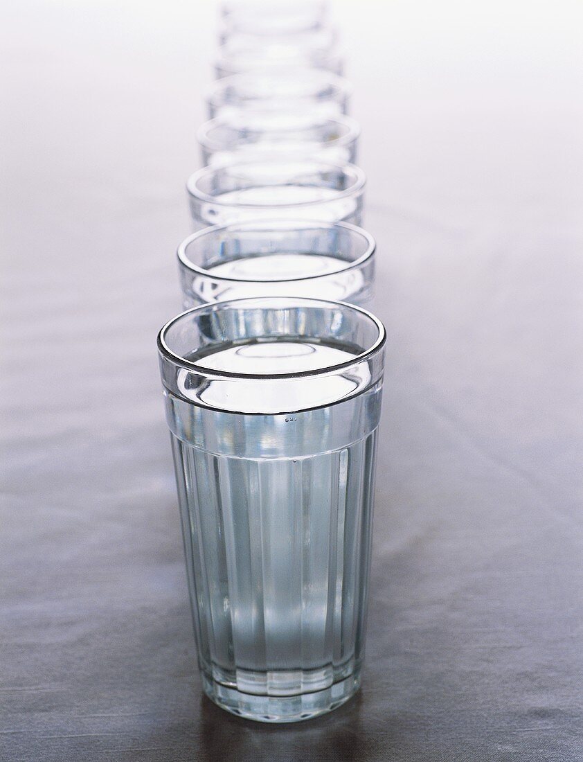 Acht Gläser Wasser in einer Reihe