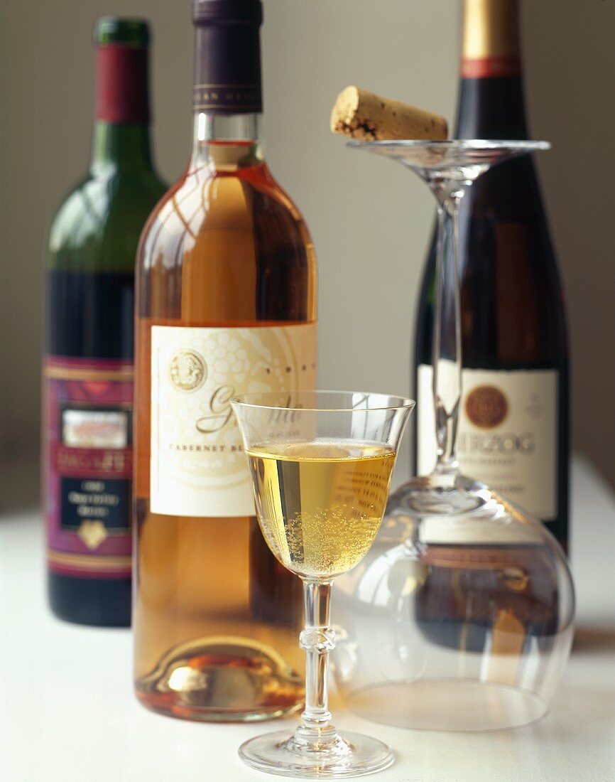 Weinflaschen, Weissweinglas und Korken auf umgekipptem Glas