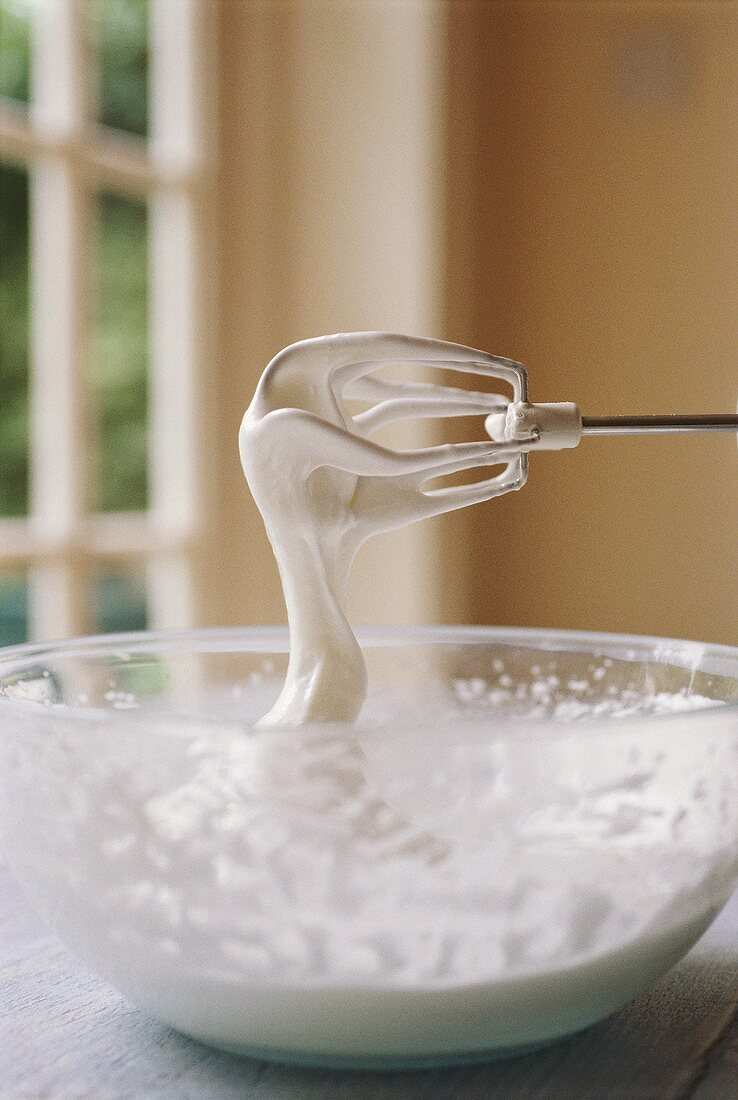 Beaten egg white in glass bowl and on beater