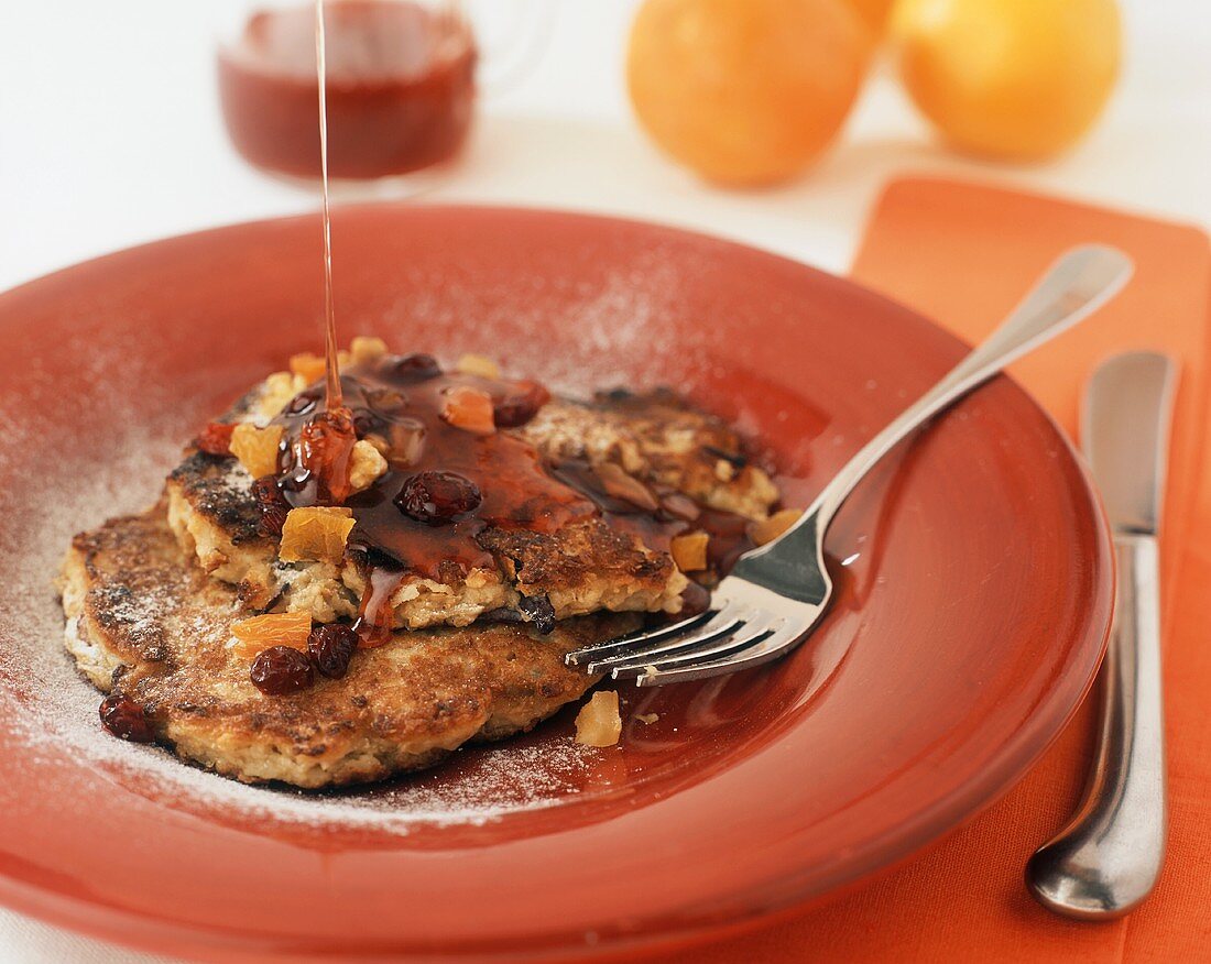 Maple Syrup Pouring on Granola Pancakes Topped with Dried Fruit