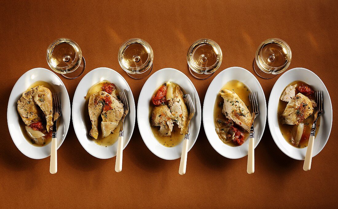 Five plates with chicken dishes and four white wine glasses