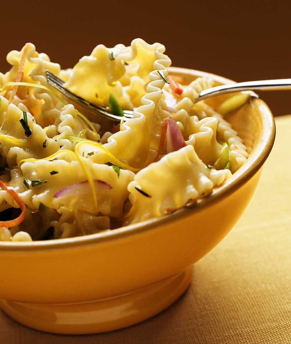 Pasta with vegetables and pine nuts in yellow bowl