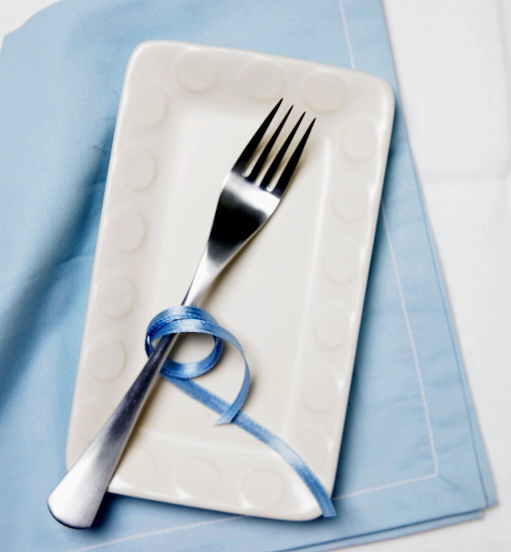 Gabel mit blauem Band auf weißem Teller und blauer Serviette