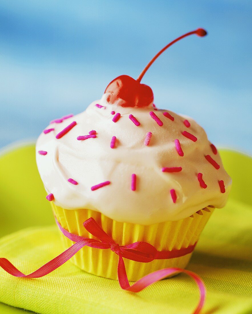 An Ice Cream Frosted Cupcake with Pink Sprinkles and a Cherry, Tied with a Ribbon