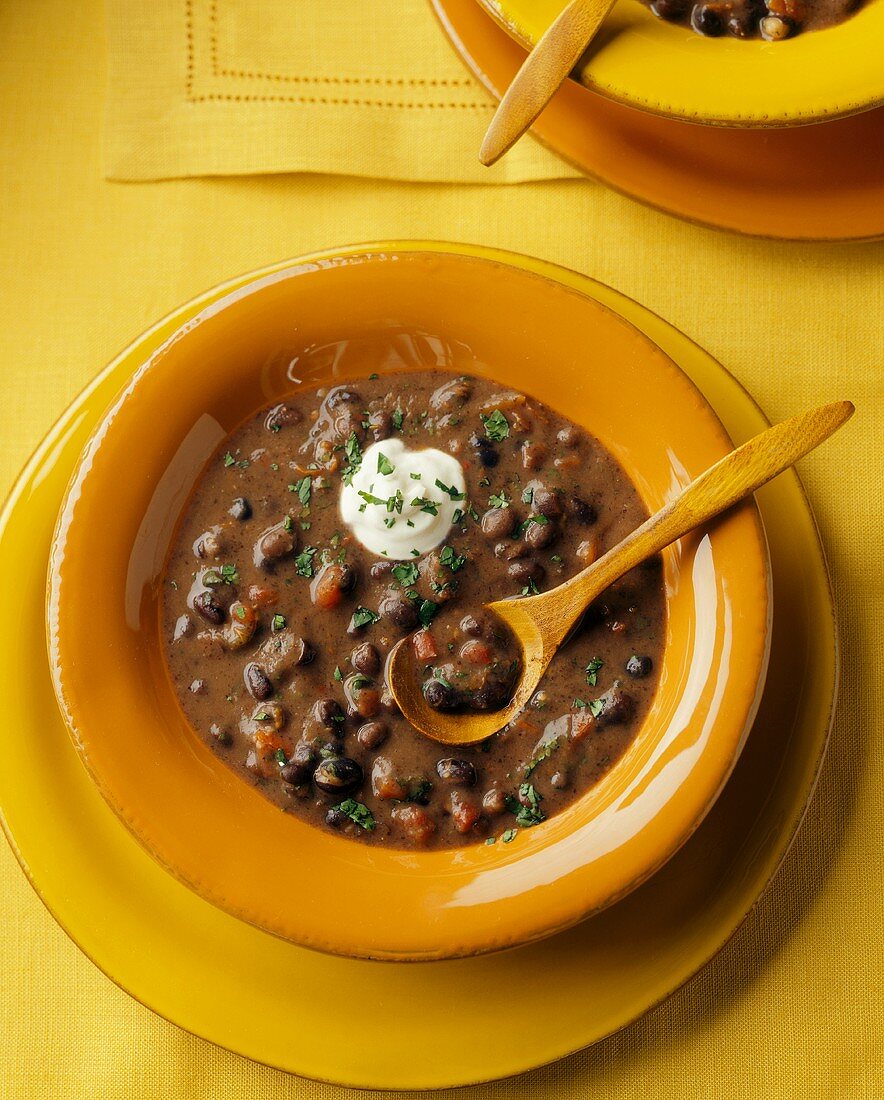 A Bowl of Black Bean Soup with Sour Cream and Cilantro and a Wooden Spoon