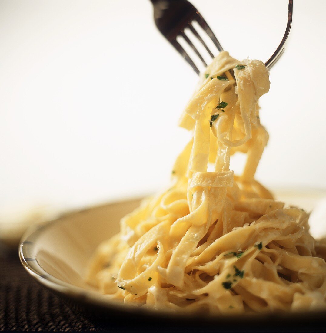 Fettuccine Alfredo Being Lifted From a Bowl by Two Forks