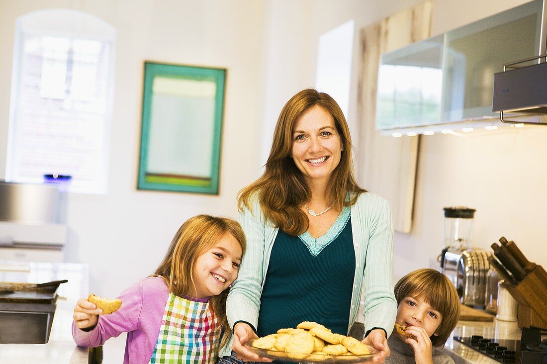 Lachende Frau mit Kindern serviert Haferplätzchen in Küche