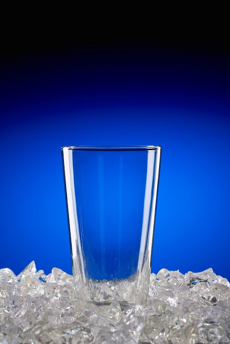 Leeres Glas auf zerstossenem Eis vor blauem Hintergrund