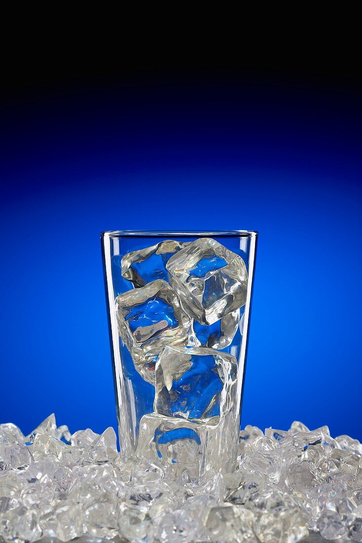 Glas mit Eiswürfeln auf Eiswürfeln vor blauem Hintergrund