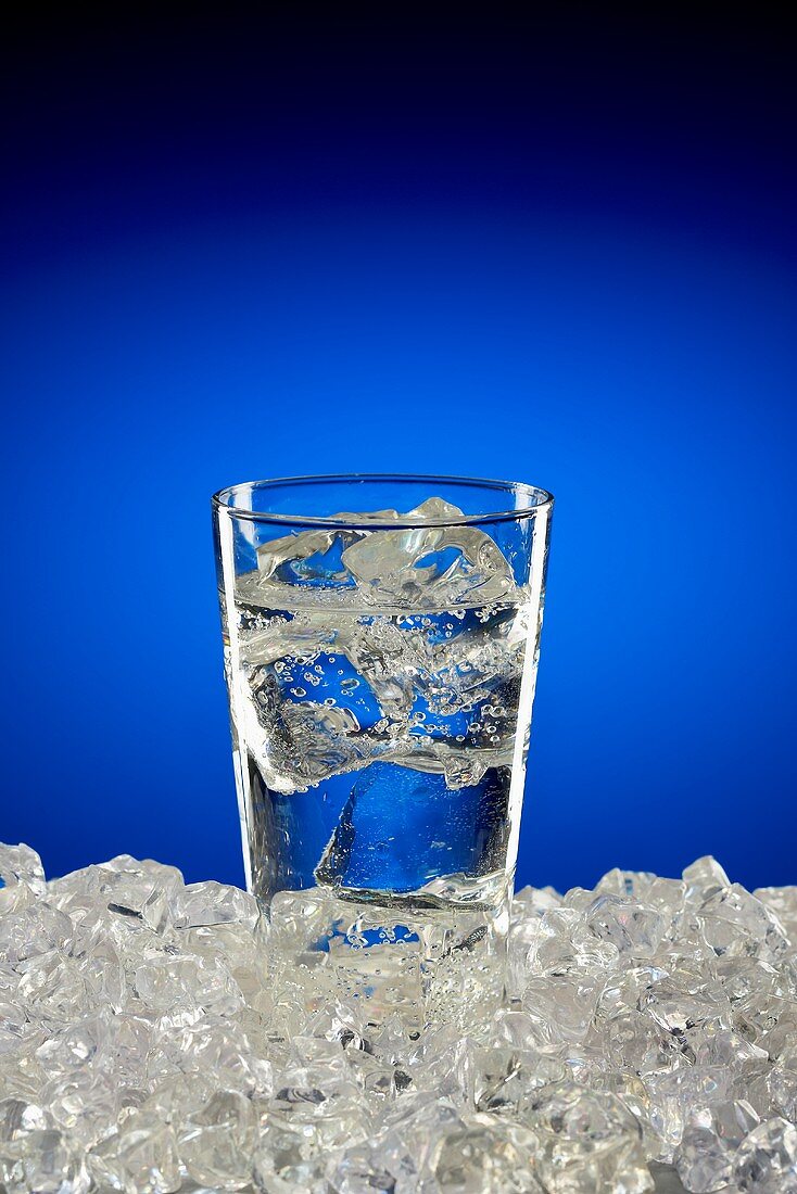 Wasserglas mit Eiswürfeln auf Eis vor blauem Hintergrund