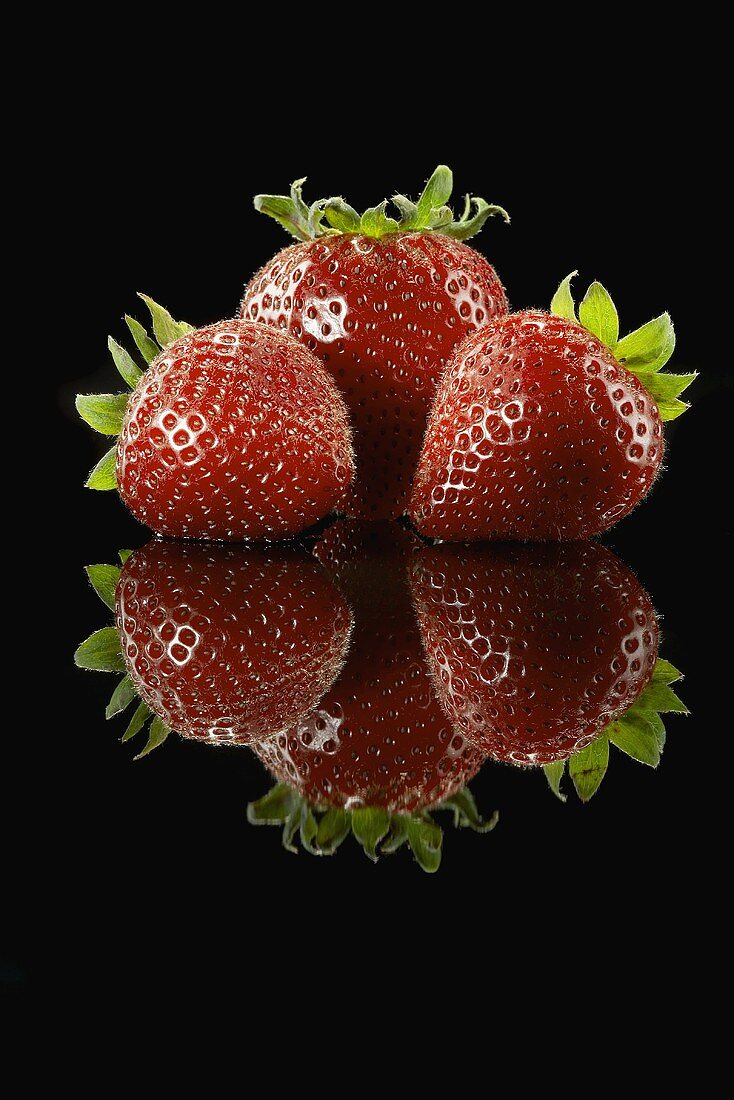 Three Ripe Strawberries on Black with Reflection