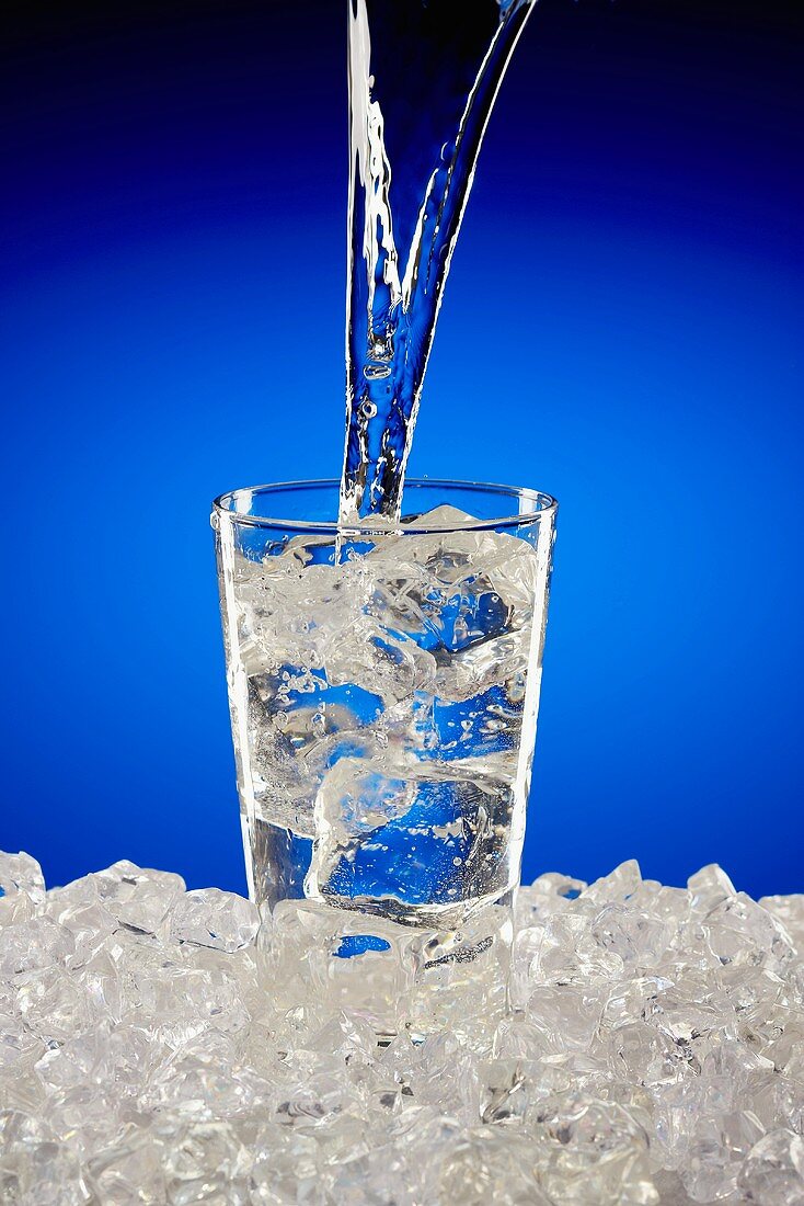 Wasser in Glas mit Eiswürfeln gießen