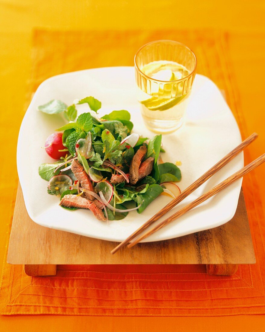 Thai Beef Salad on a Square Plate with Chopsticks and Water with Lime
